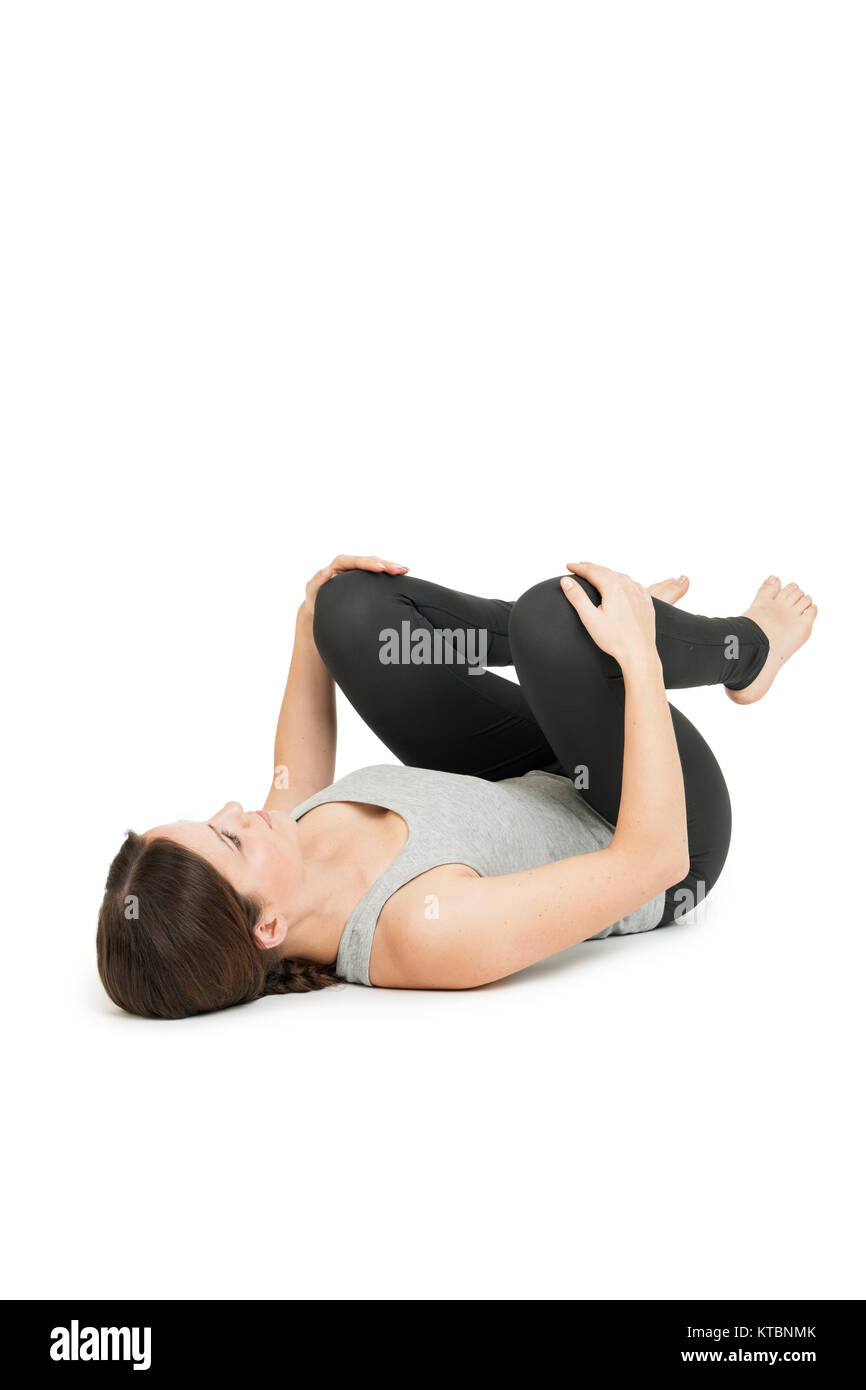 Flachwinkelige Ganzkörper-Ansicht einer auf dem Rücken liegenden jungen Frau in der Yogaposition 'glückliches Baby' (anada balasana) auf weißem Hintergrund. Stock Photo