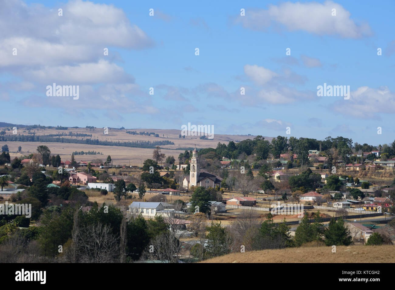 View of small town with church in the middle and farming land around the town with green trees, white cloudy and blue sky Stock Photo
