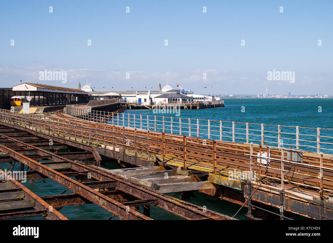 S view of Ryde pier with rusty rails in the foreground and Portsmouth in the distance on a sunny day with blue skies. Stock Photo