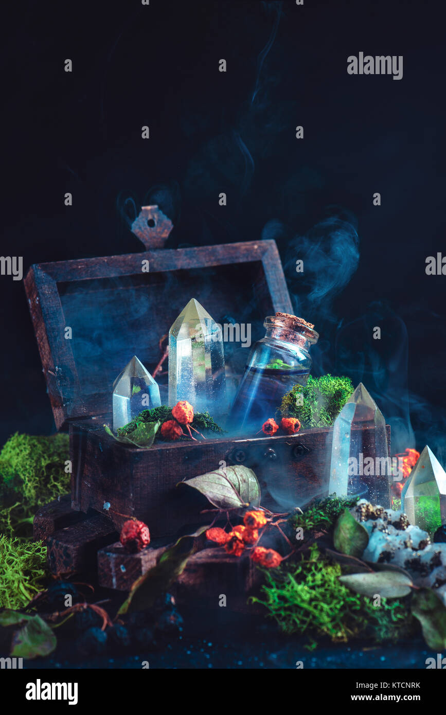 Magical still life with a wooden chest, potion bottle, crystals, moss, berries and leaves on a dark background. Modern witchcraft concept with copy sp Stock Photo