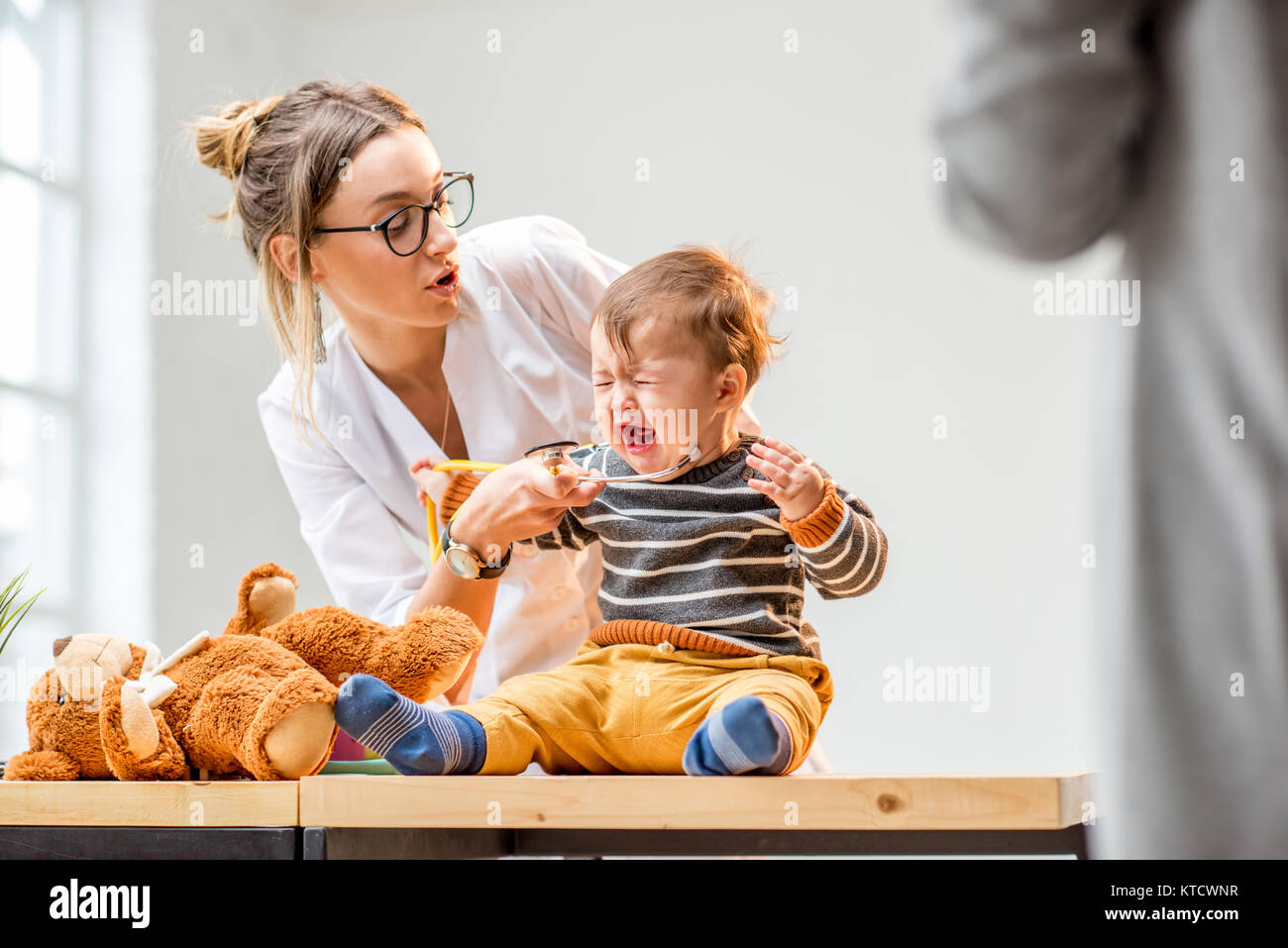 Young woman pediatrician taking care of a baby boy sitting on the table at the office Stock Photo