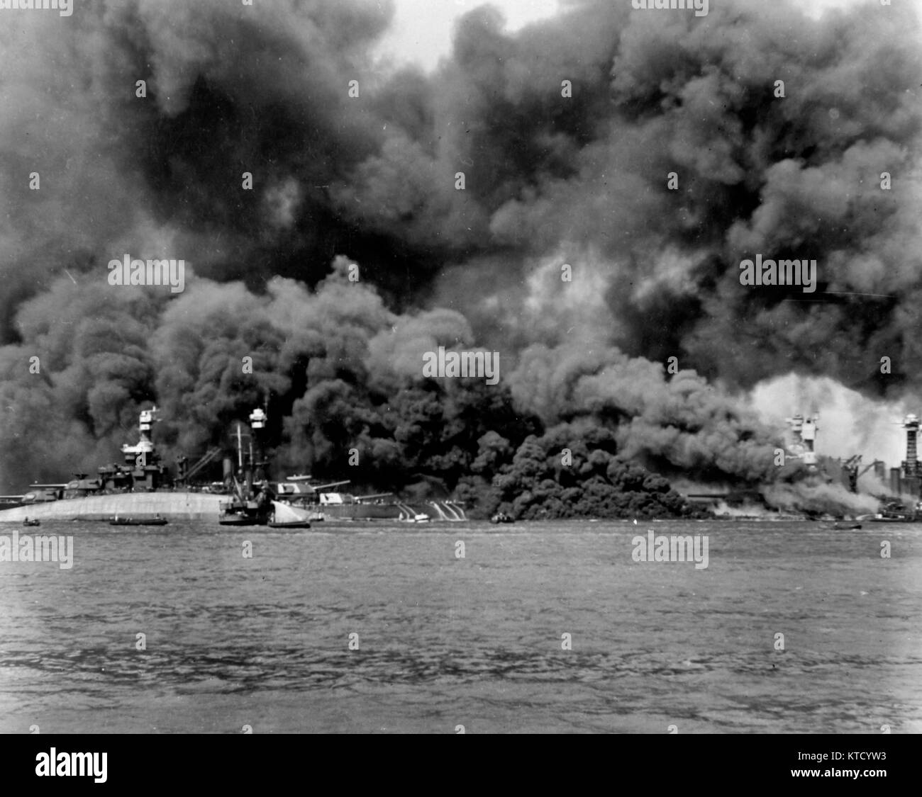 Pearl Harbor Attack, 7 December 1941 -  View of Battleship Row during or immediately after the Japanese raid. USS West Virginia (BB-48) is at the right sunk alongside USS Tennessee (BB-43), with oil fires shrouding them both. The capsized USS Oklahoma (BB-37) is at the left, alongside USS Maryland (BB-46). Crewmen on the latter's stern are using firehoses to try to push burning oil away from their ship. Stock Photo