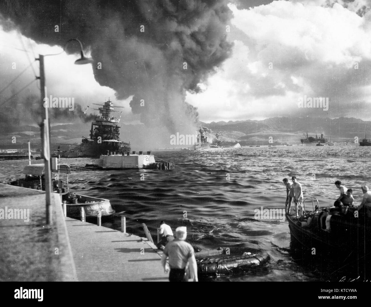 Pearl Harbor Attack, 7 December 1941 - View looking down Battleship Row from Ford Island Naval Air Station, shortly after the Japanese torpedo plane attack. USS California (BB-44) is at left, listing to port after receiving two torpedo hits. In the center are USS Maryland (BB-46) with the capsized USS Oklahoma (BB-37) alongside. USS Neosho (AO-23) is at right, backing clear of the area. Most smoke is from USS Arizona (BB-39). Stock Photo