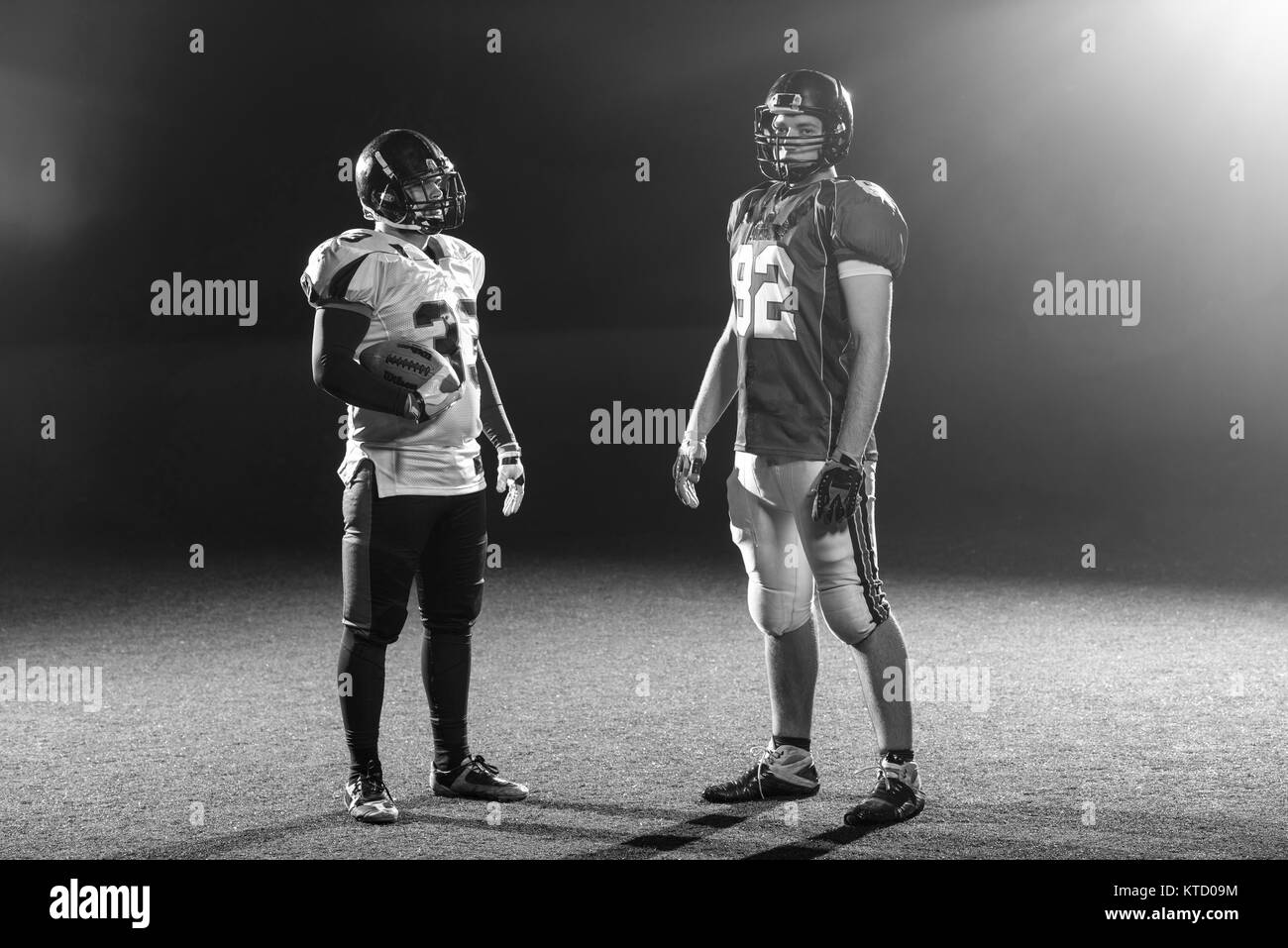 portrait of confident American football players holding ball while standing on field at night Stock Photo