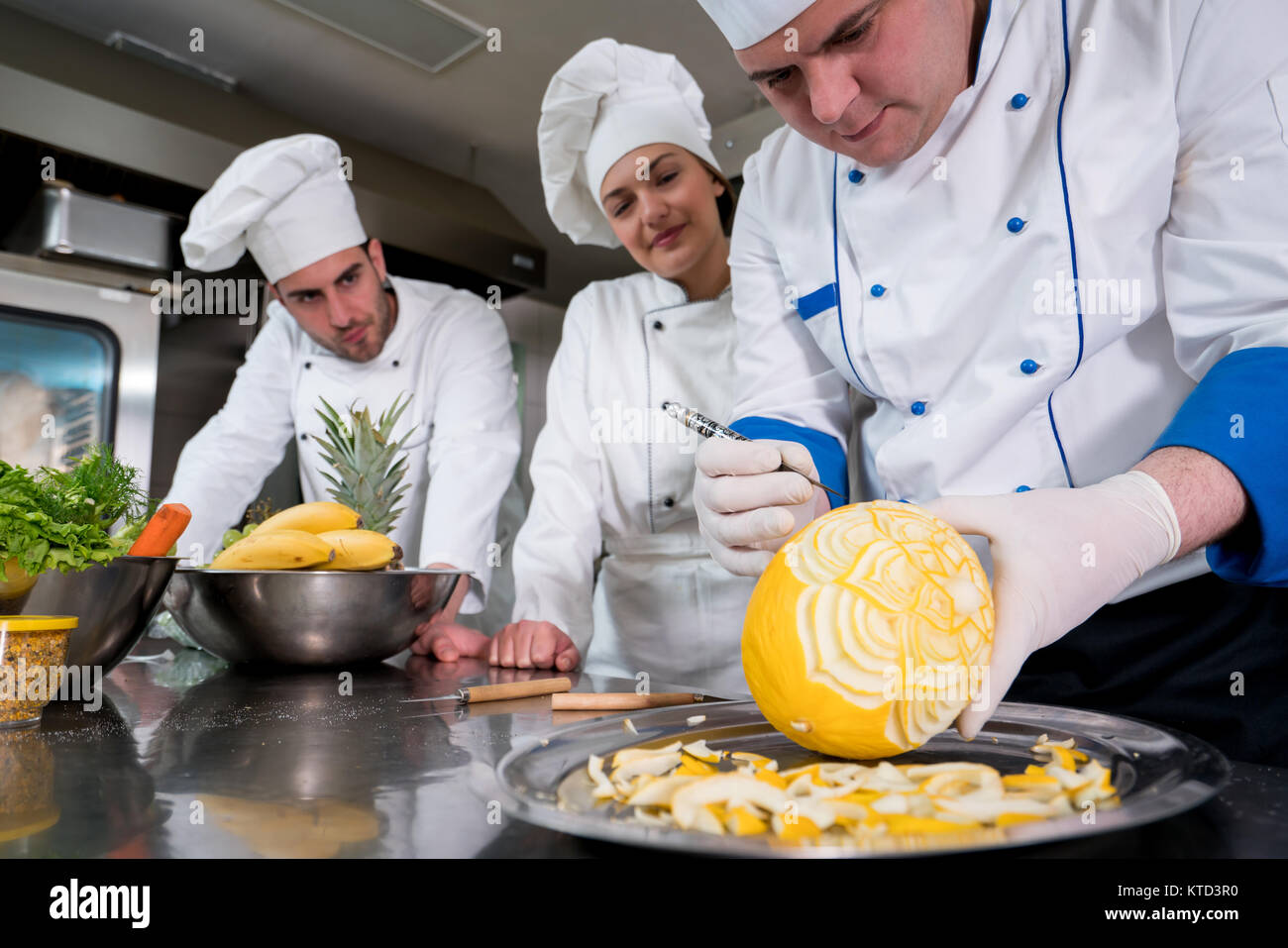 Kitchen chef with young apprentices, teaching to make decorative fruit basket Stock Photo