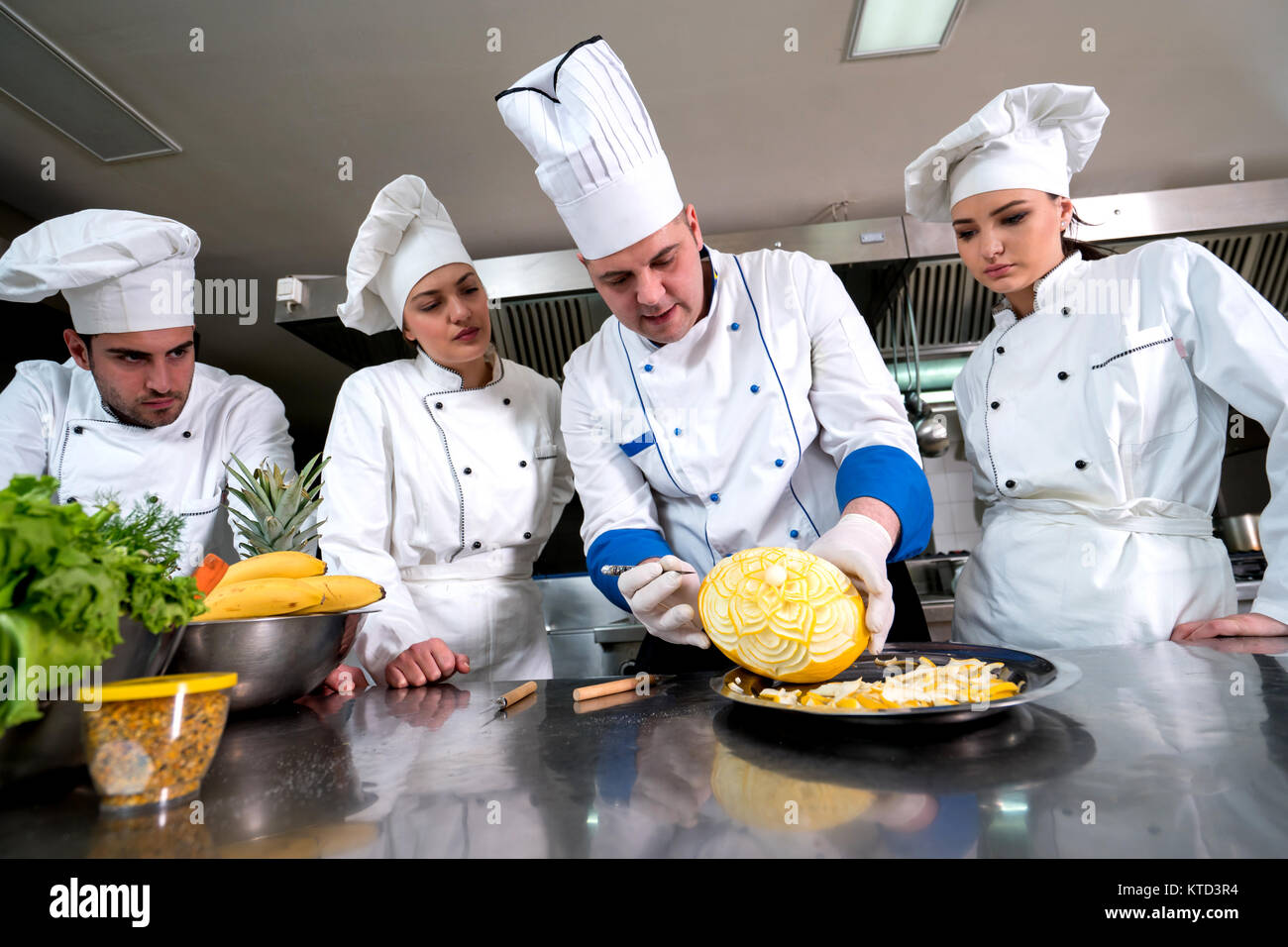 Kitchen chef with young apprentices, teaching to make decorative fruit basket Stock Photo