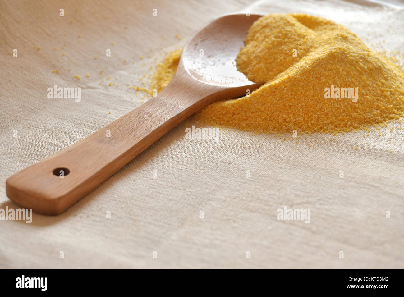 Pile of organic corn grits and a wooden spoon on coarse cloth. Prepared ingredient for cooking. Stock Photo