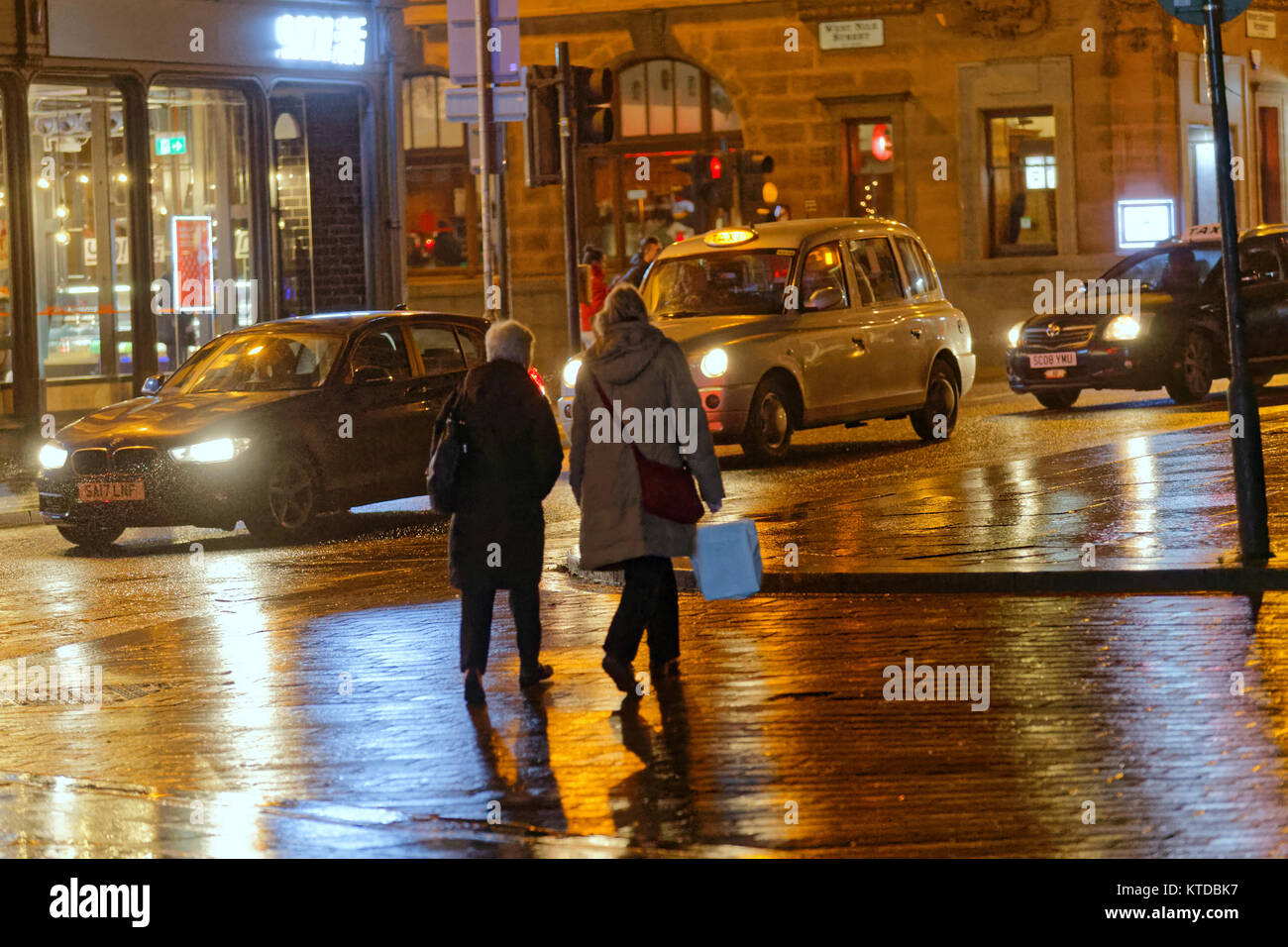 gritty urban night time Glasgow wet street life women mother and daughter returning home walking on street bags  taxi a shopping trip late at night Stock Photo