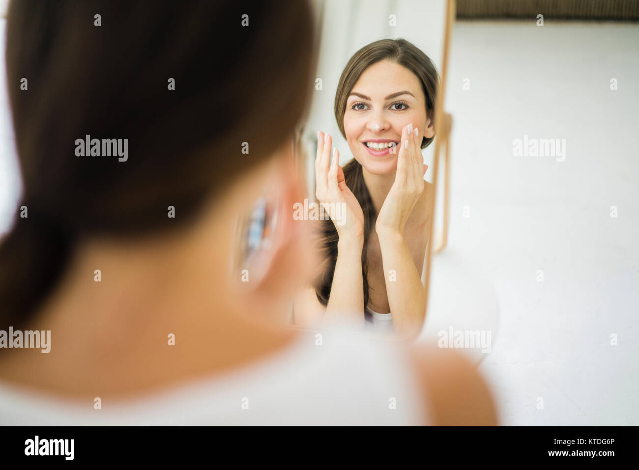 Portrait of woman looking at her mirror image in the morning creaming her face Stock Photo