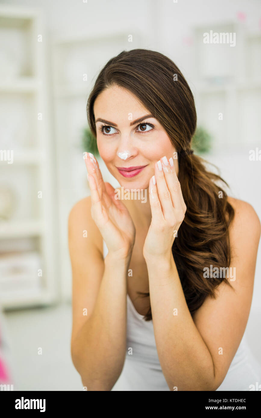 Portrait of smiling young woman creaming her face Stock Photo
