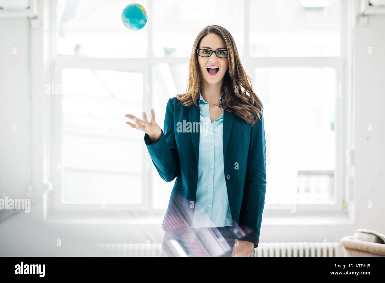 Portrait of businesswoman throwing small globe in the air Stock Photo