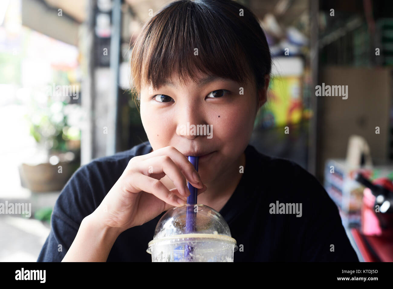 Asian pretty girl drinking smoothie in the street and looking at camera. Chiang Mai, Thailand. Stock Photo