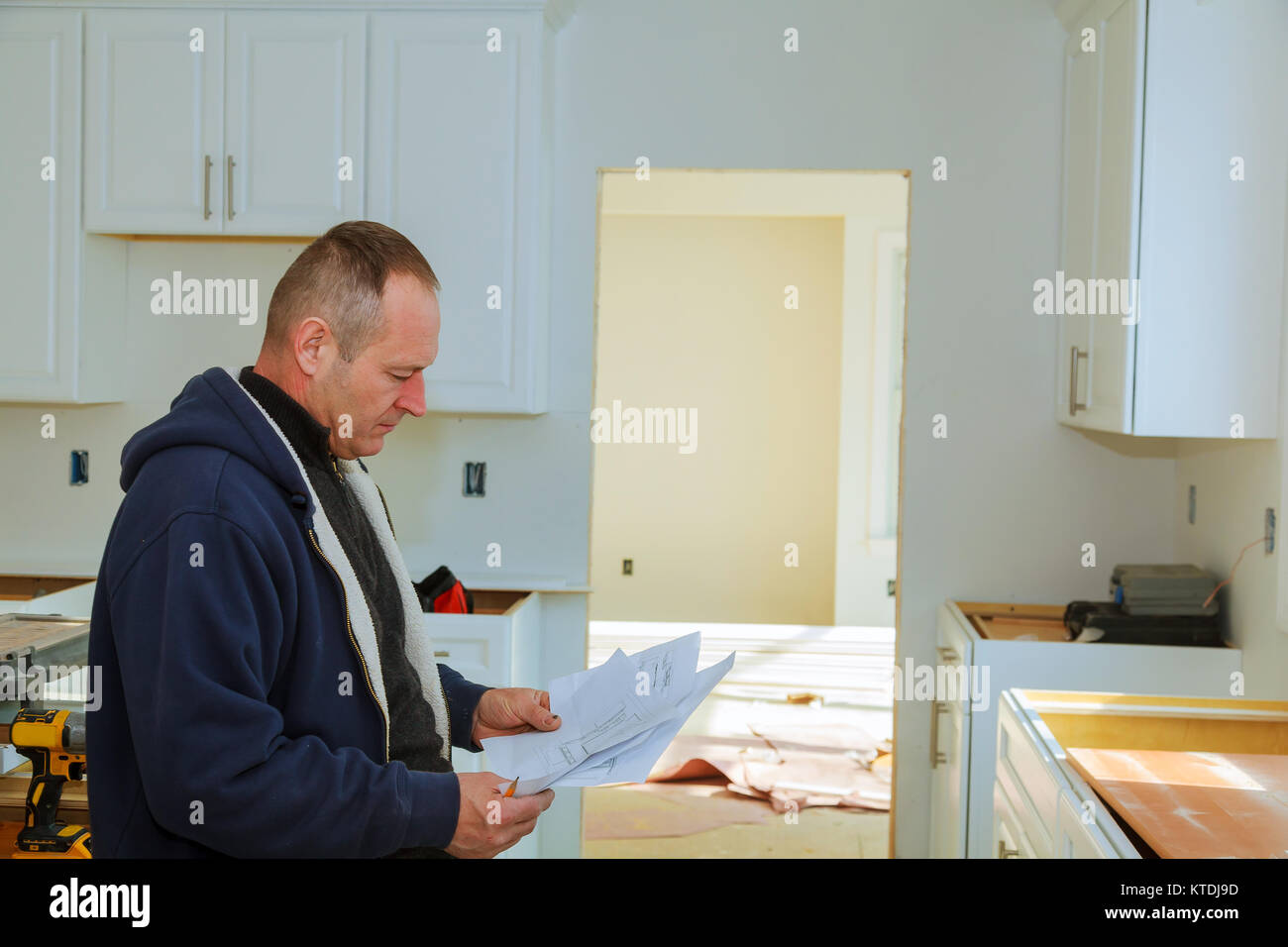 the worker keeps a plan for installing the kitchen cabinets Carpenter working on new kitchen cabinets Stock Photo