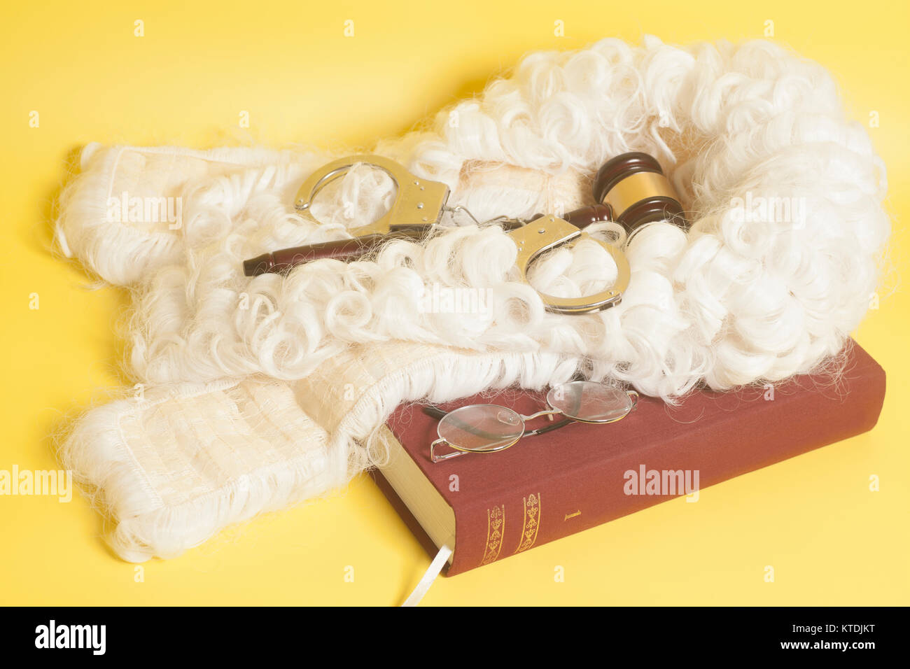 set for judge:judge wig,handcuffs, judge gavel,book end eyeglasses on yellow background Stock Photo