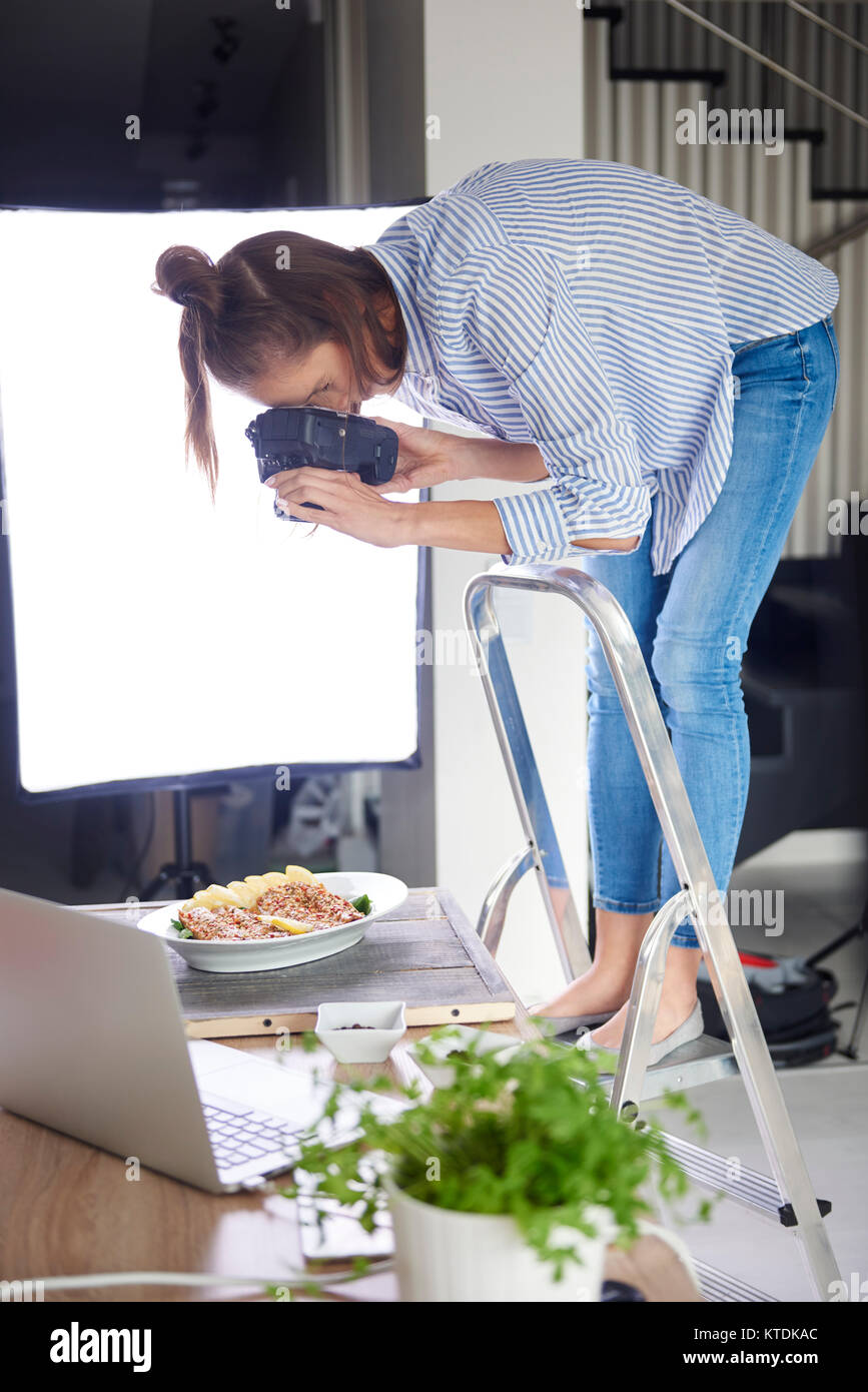 Woman standing on step ladder and photographing food Stock Photo