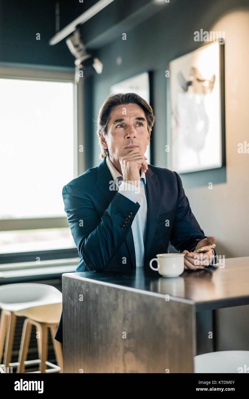 Businessman in cafeteria with cup of coffee thinking Stock Photo