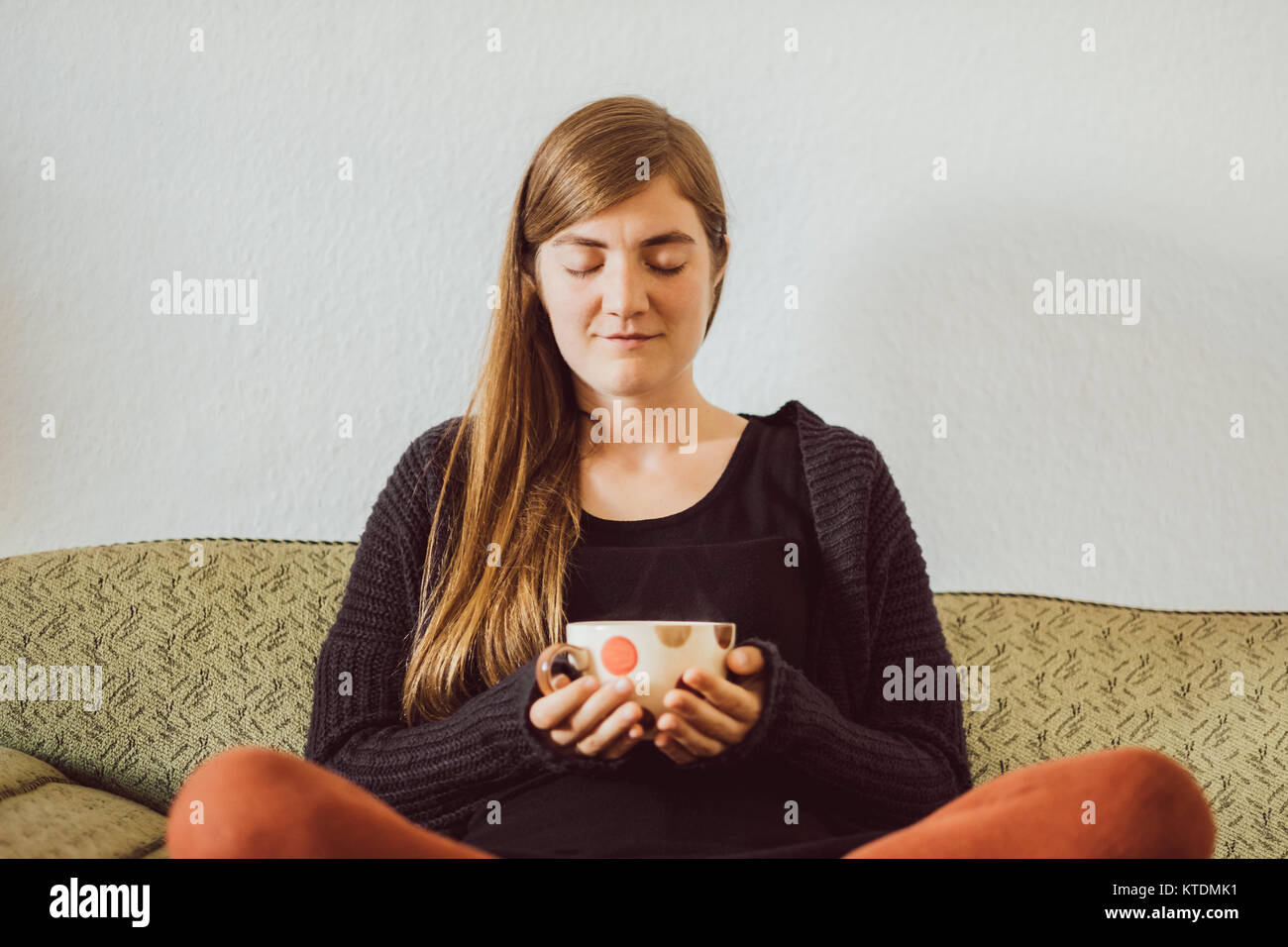 Woman with eyes closed sitting on couch with tea cup Stock Photo - Alamy
