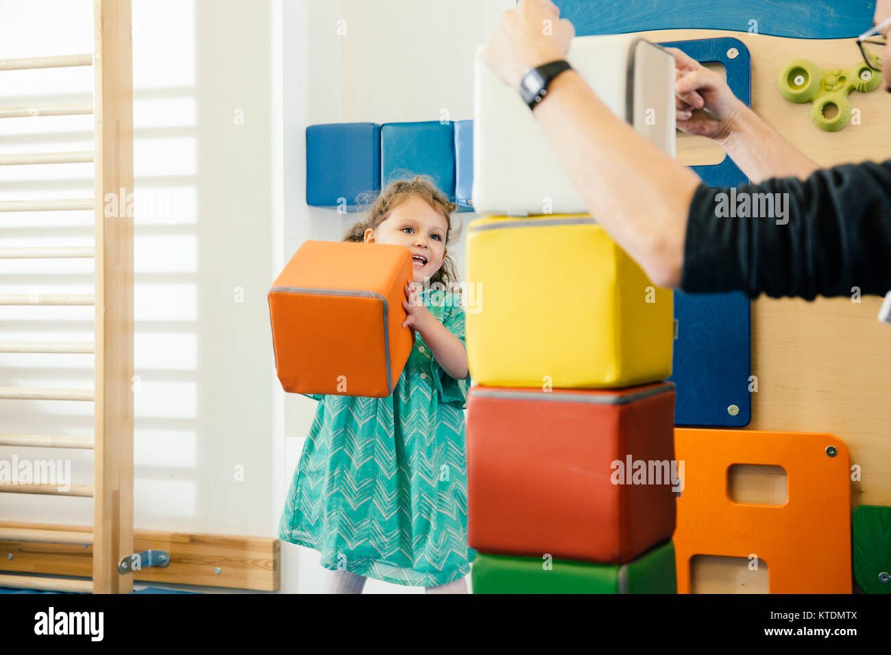 Happy little girl lifting up a soft building block in gym room of a kindergarten Stock Photo