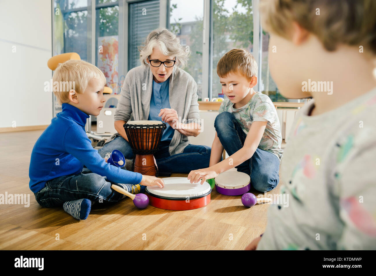 Children using percussion instruments with instructor in music room of