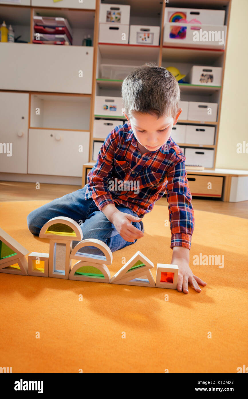 Boy lining up wooden toy shapes on carpet in kindergarten Stock Photo