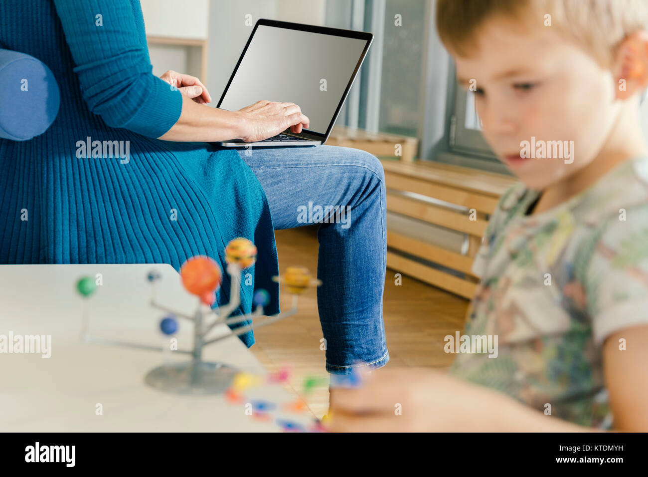 Boy exploring solar system model with woman with laptop in kindergarten Stock Photo