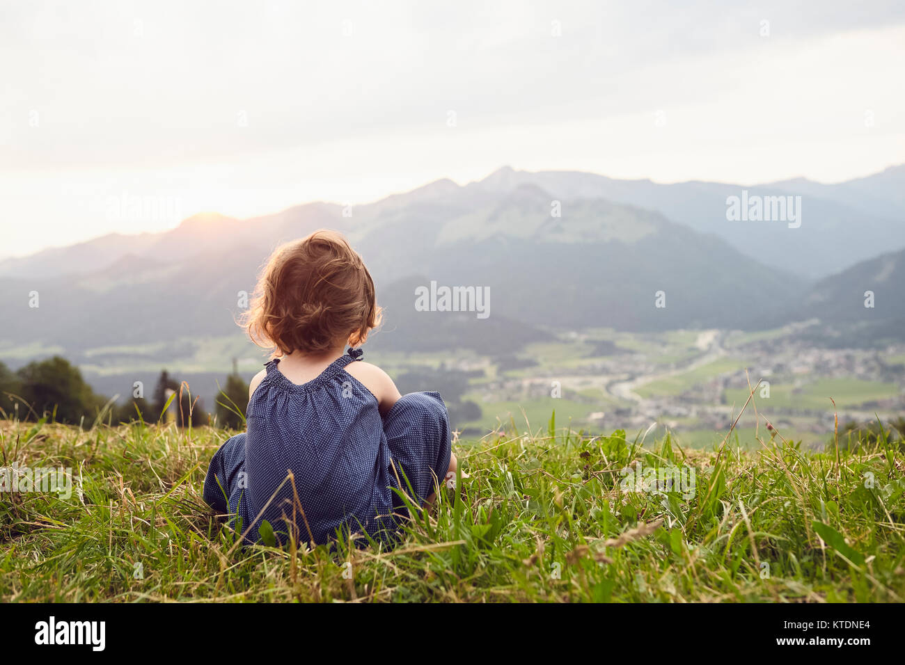 Austria, Tyrol, back view of little girl sitting on Alpine meadow looking at view Stock Photo