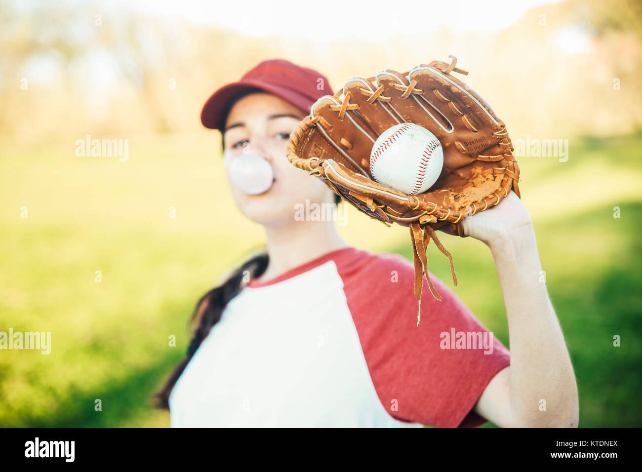 Portrait of young woman with ball and baseball glove blowing a gum bubble Stock Photo