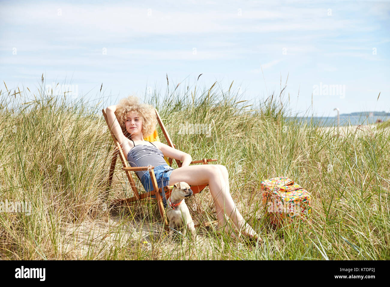 Portrait of young woman sitting on beach chair in the dunes watching ...