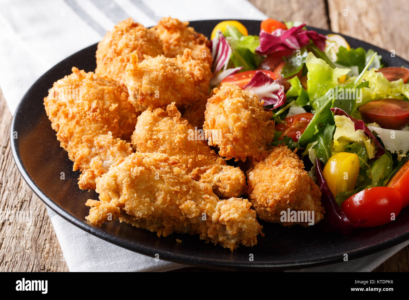 deep-fried chicken wings in breadcrumbs and fresh salad close-up on a plate on a table. horizontal Stock Photo