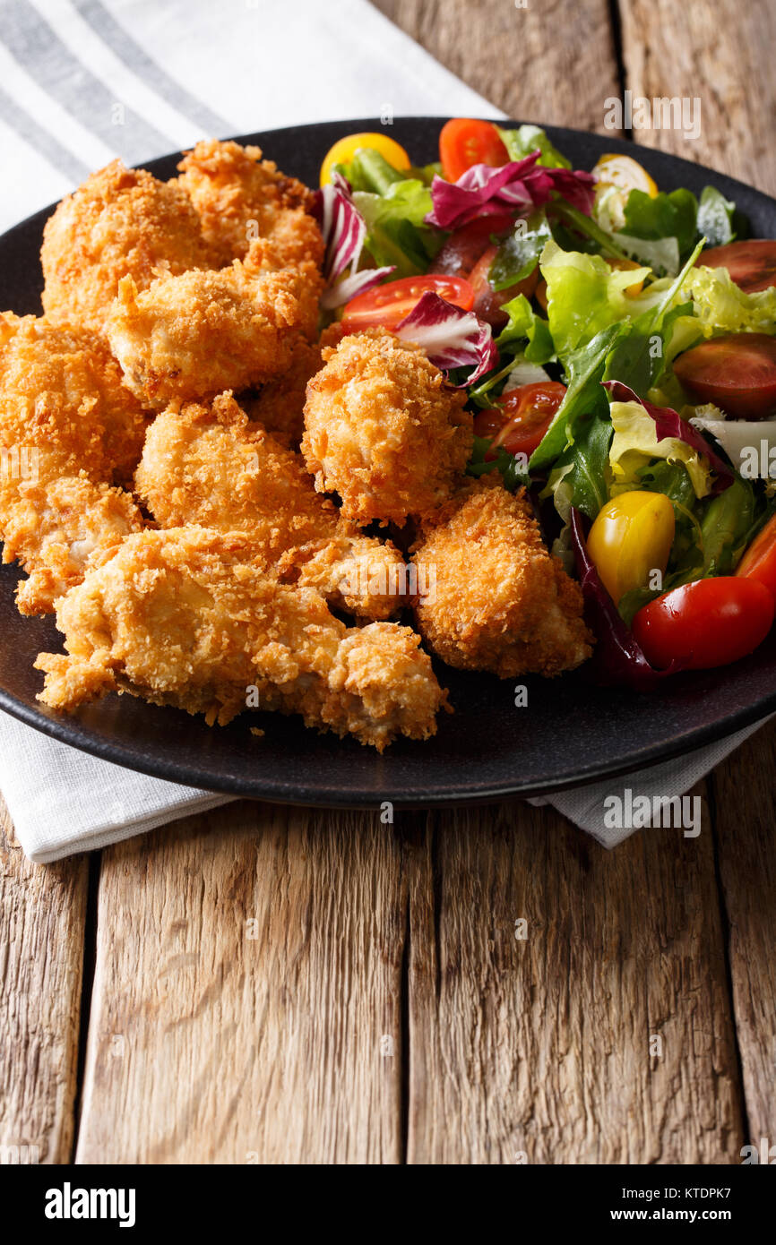 Crispy chicken wings in breadcrumbs and fresh salad close-up on a plate on a table. vertical Stock Photo