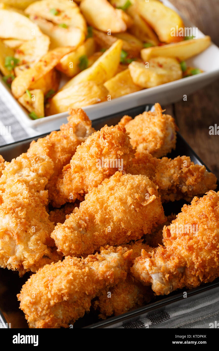 Fried chicken wings in breadcrumbs and potato slices close-up on a plate. vertical Stock Photo