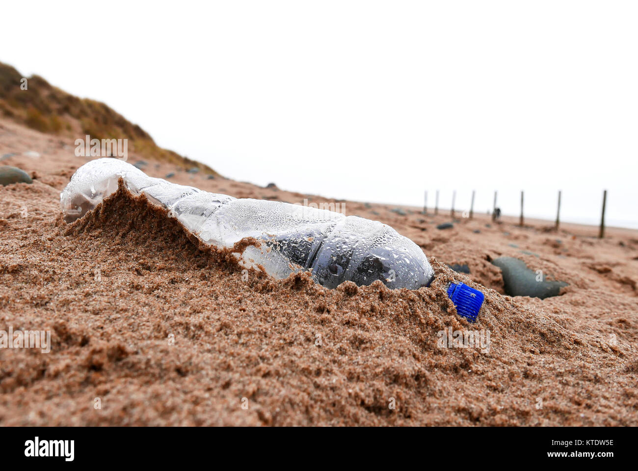 abandoned plastic water bottle left on beach and covered with sand Stock Photo