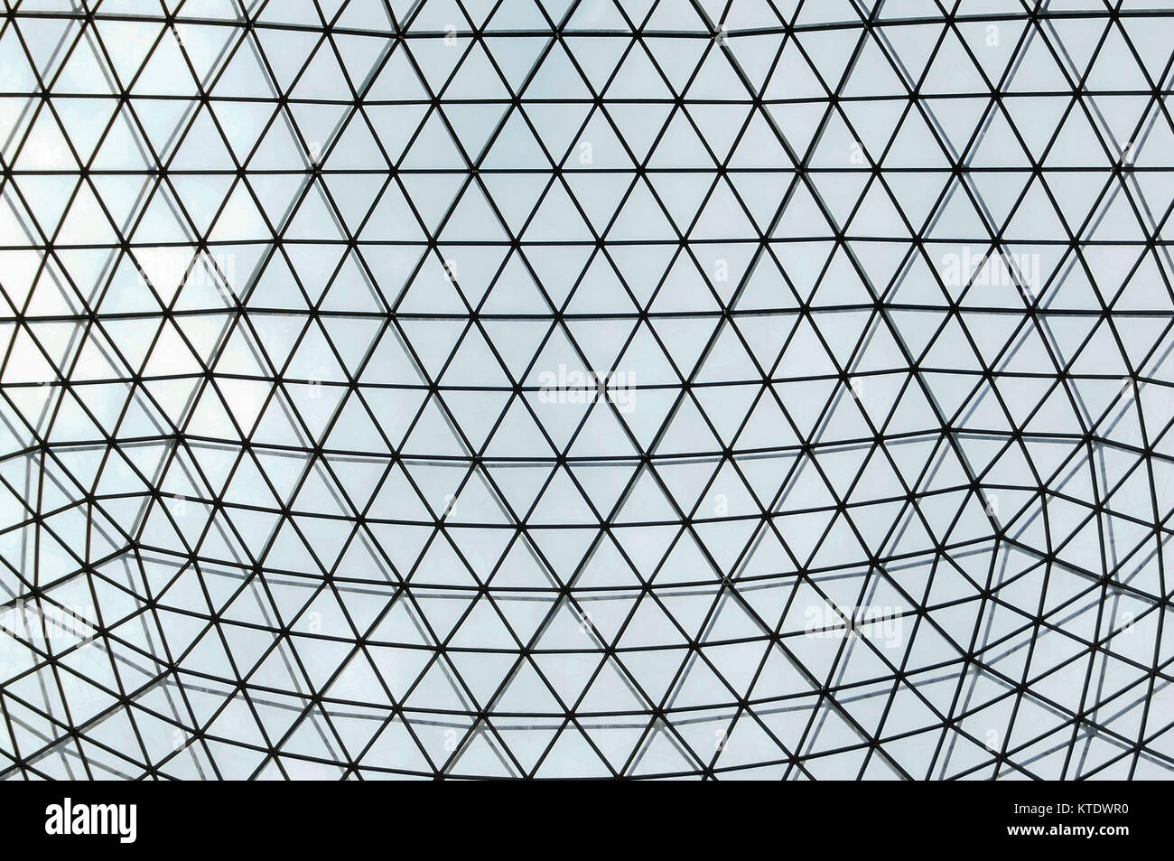 metal and glass atrium roof in repeating symmetrical triangualar pattern, shown with light coming through Stock Photo
