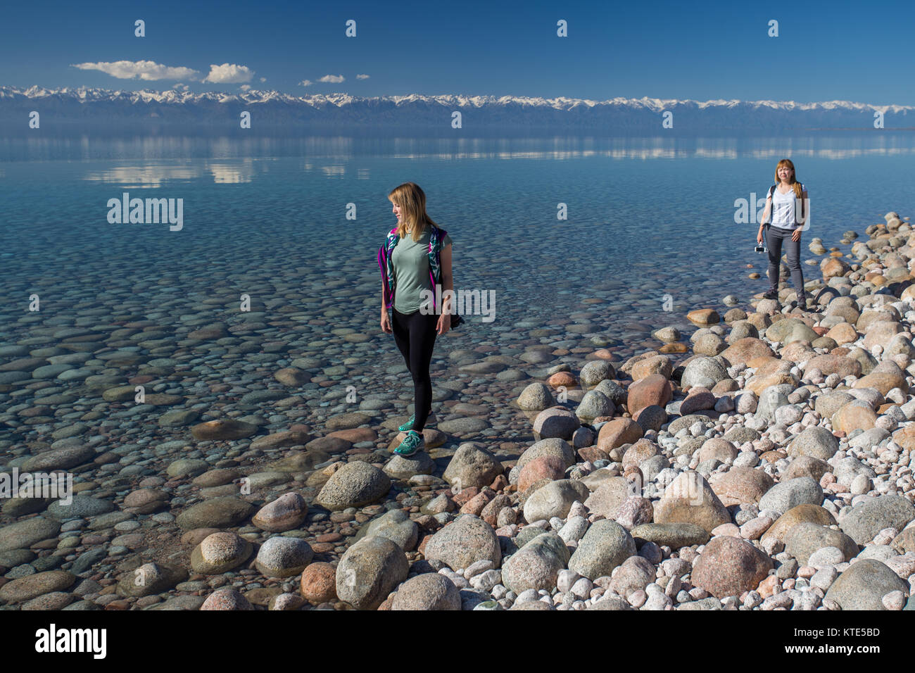 Two mid-20s female tourists walking along the southern shore of Issyk-Kol lake in Kyrgyzstan. Stock Photo