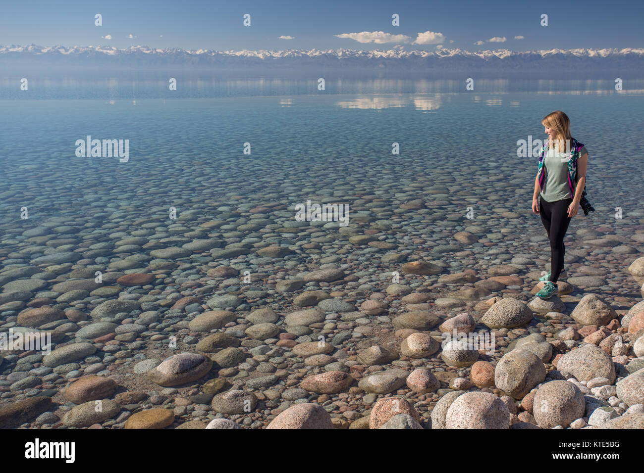 A female model on the southern shore of Issyk-Kol in Kyrgyzstan, with the mountains of the north shore reflected in the background. Stock Photo