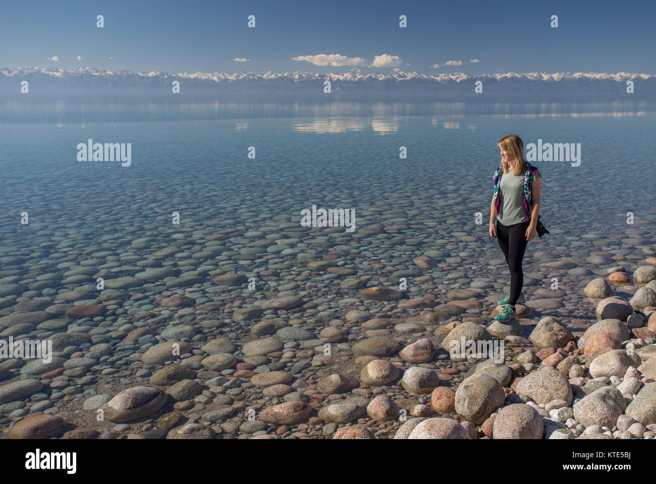 A female model on the southern shore of Issyk-Kol in Kyrgyzstan, with the mountains of the north shore reflected in the background. Stock Photo
