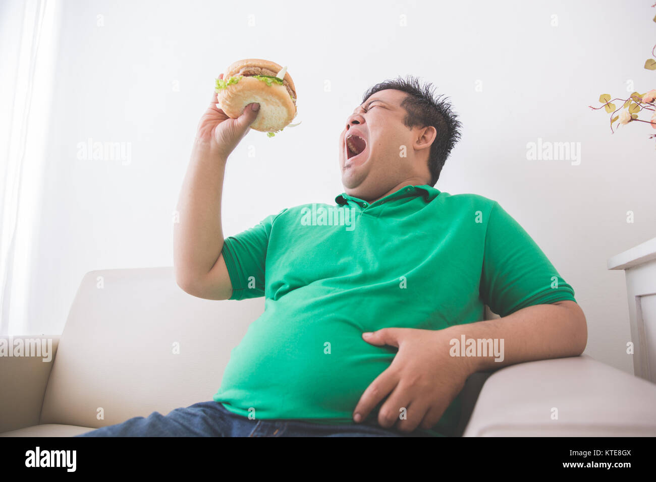 Overweight man eating hamburger at home Stock Photo