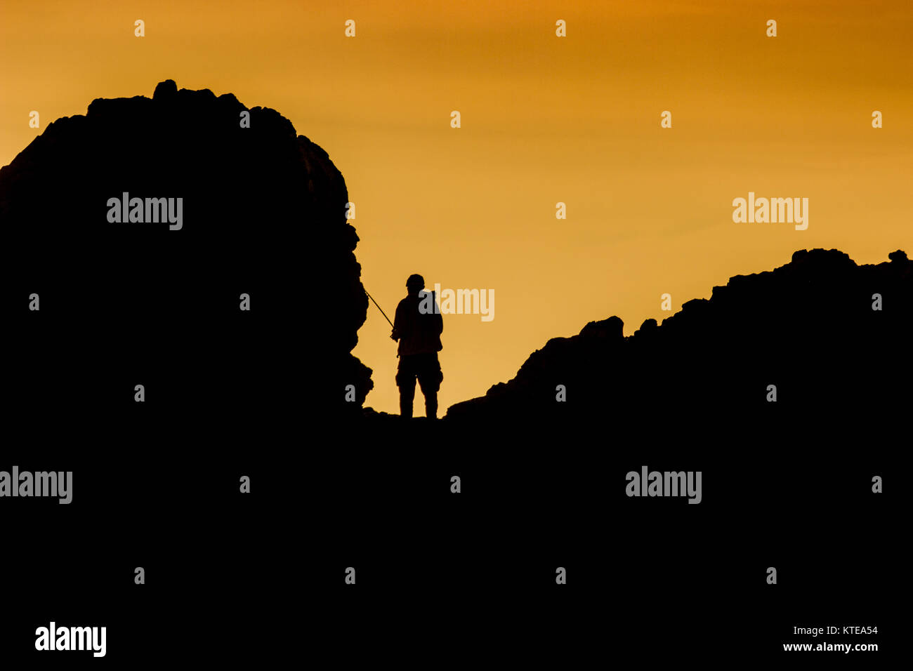 Silhouette of fisherman standing on a rock formation at sunset from Little Corona Beach, Corona Del Mar, California Stock Photo