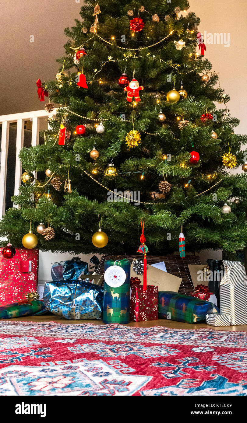 Wrapped Christmas presents under a Christmas tree in a family sitting room with a Persian rug Stock Photo