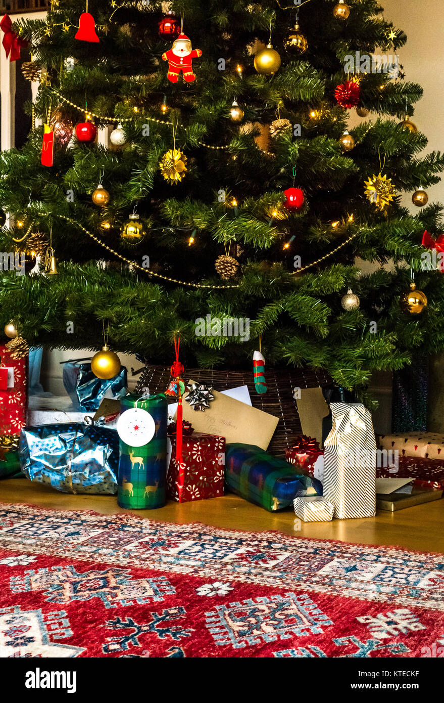 Wrapped Christmas presents under a Christmas tree in a family sitting room with a Persian rug Stock Photo