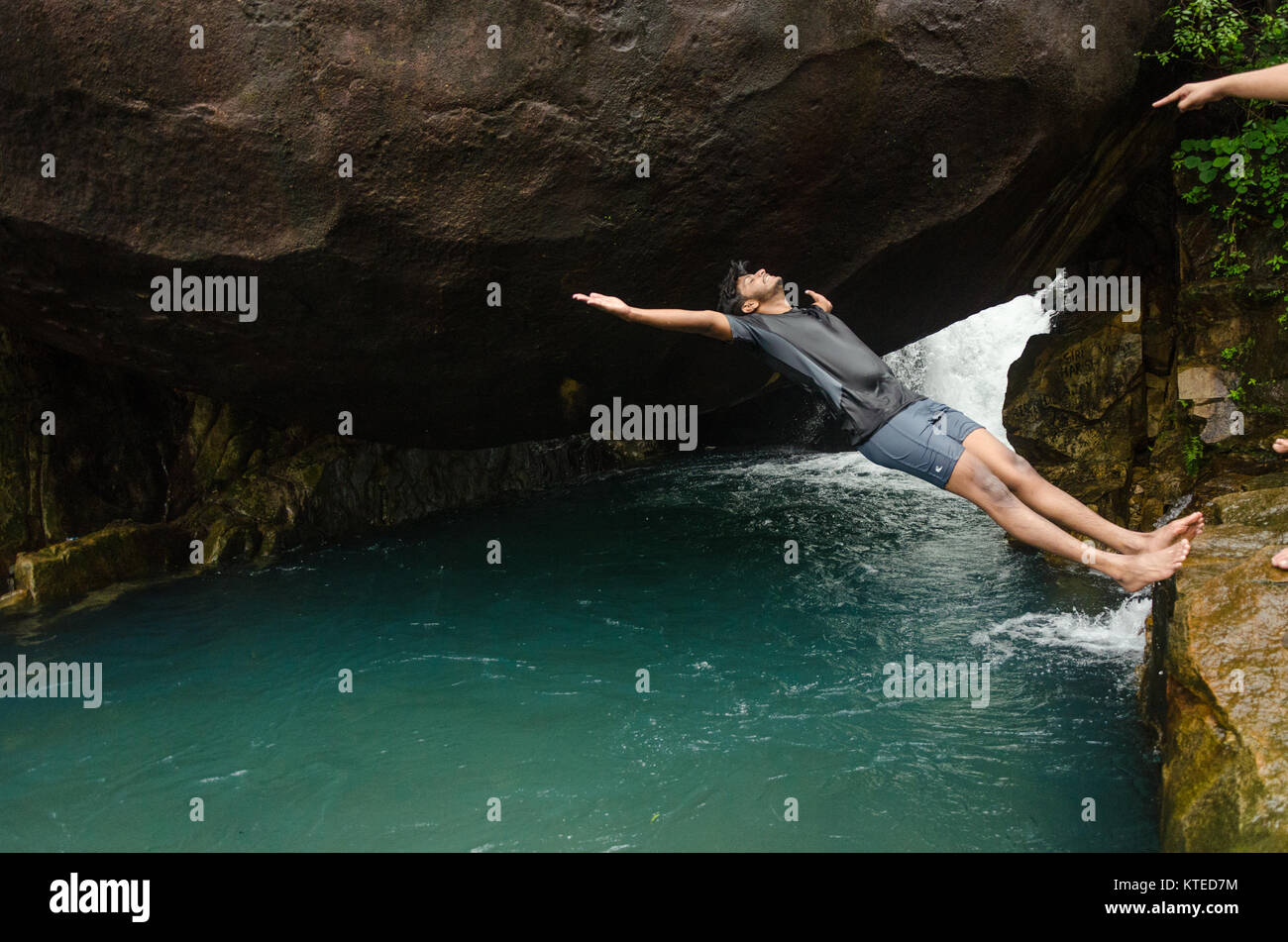 Young adult boy about to fall in reverse off a cliff after a push from his friends at Nagarmadi Water Falls, Chendia, Karnataka, India Stock Photo