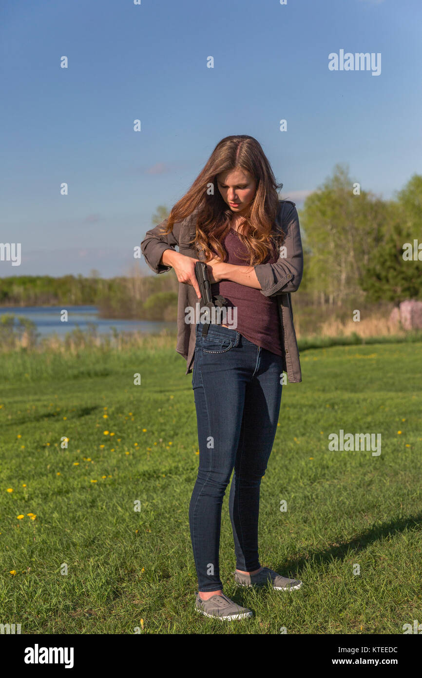 Young woman places her pistol in a conceal carry waistband. Stock Photo