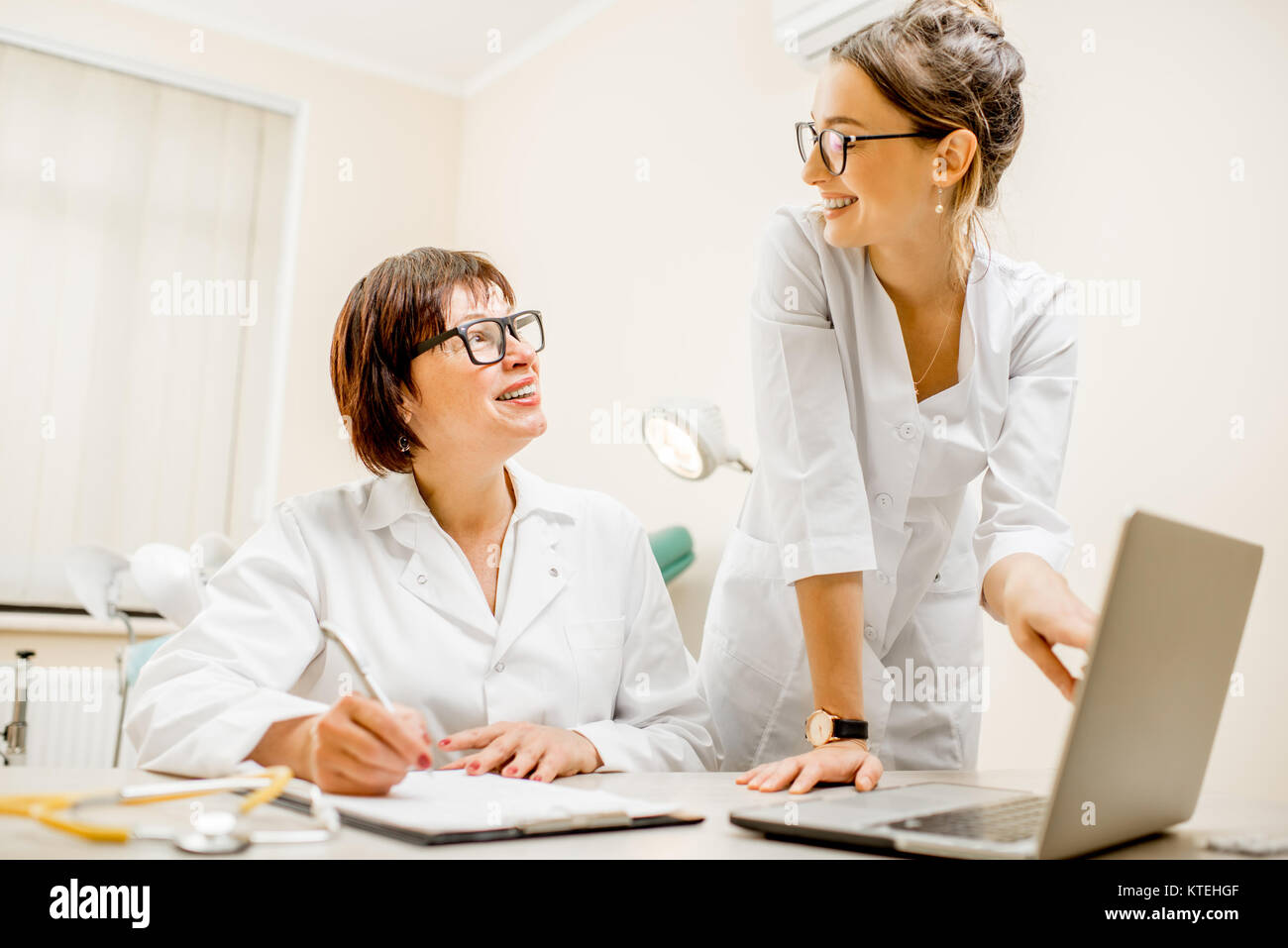 Senior doctor and young woman assistant working together with laptop ...