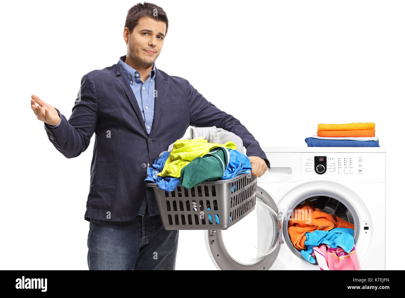 Unhappy elegant guy holding a laundry basket filled with clothes in front of a washing machine isolated on white background Stock Photo