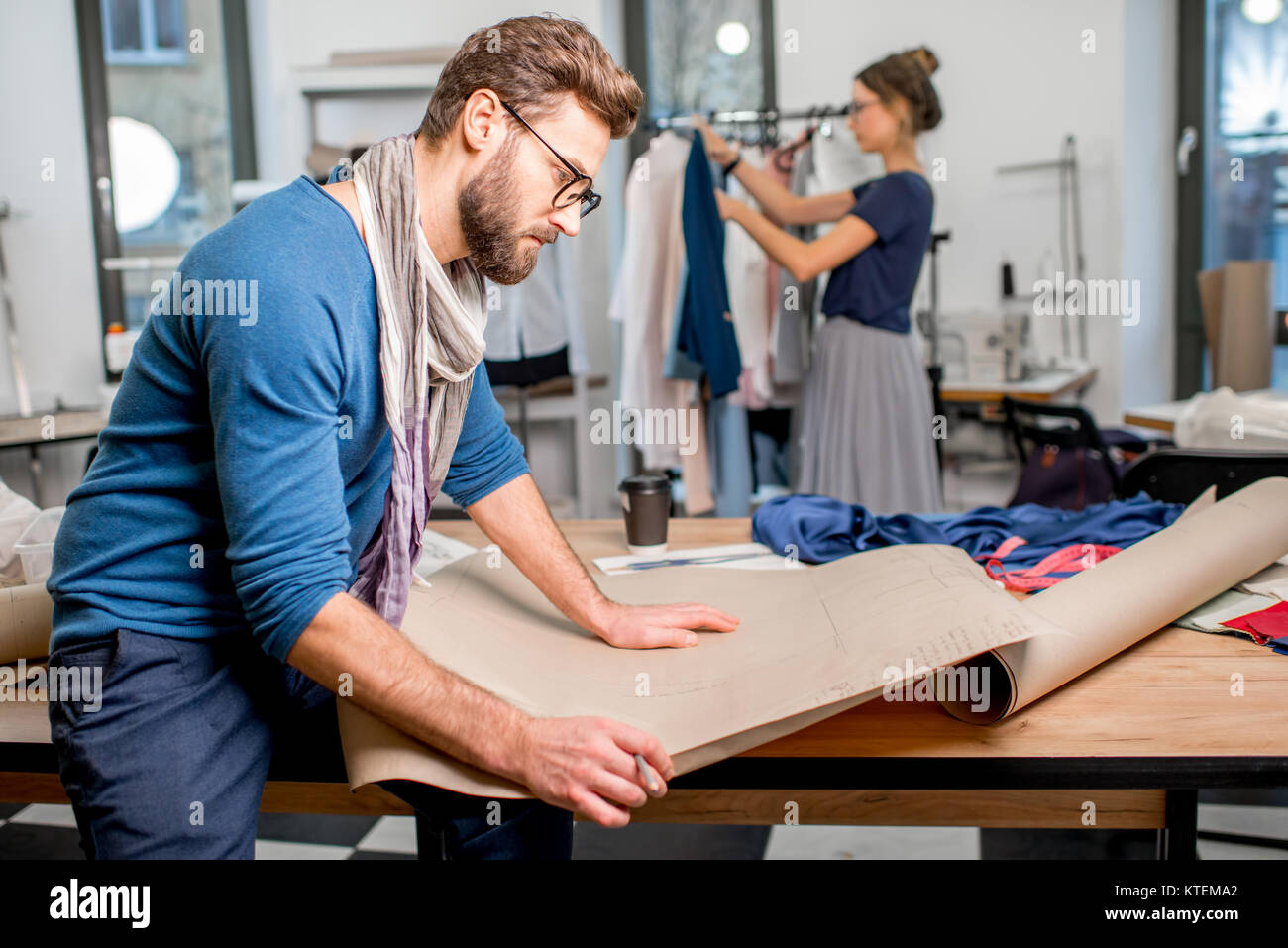Portrait of a handsome fashion designer sitting with paper sketches at ...