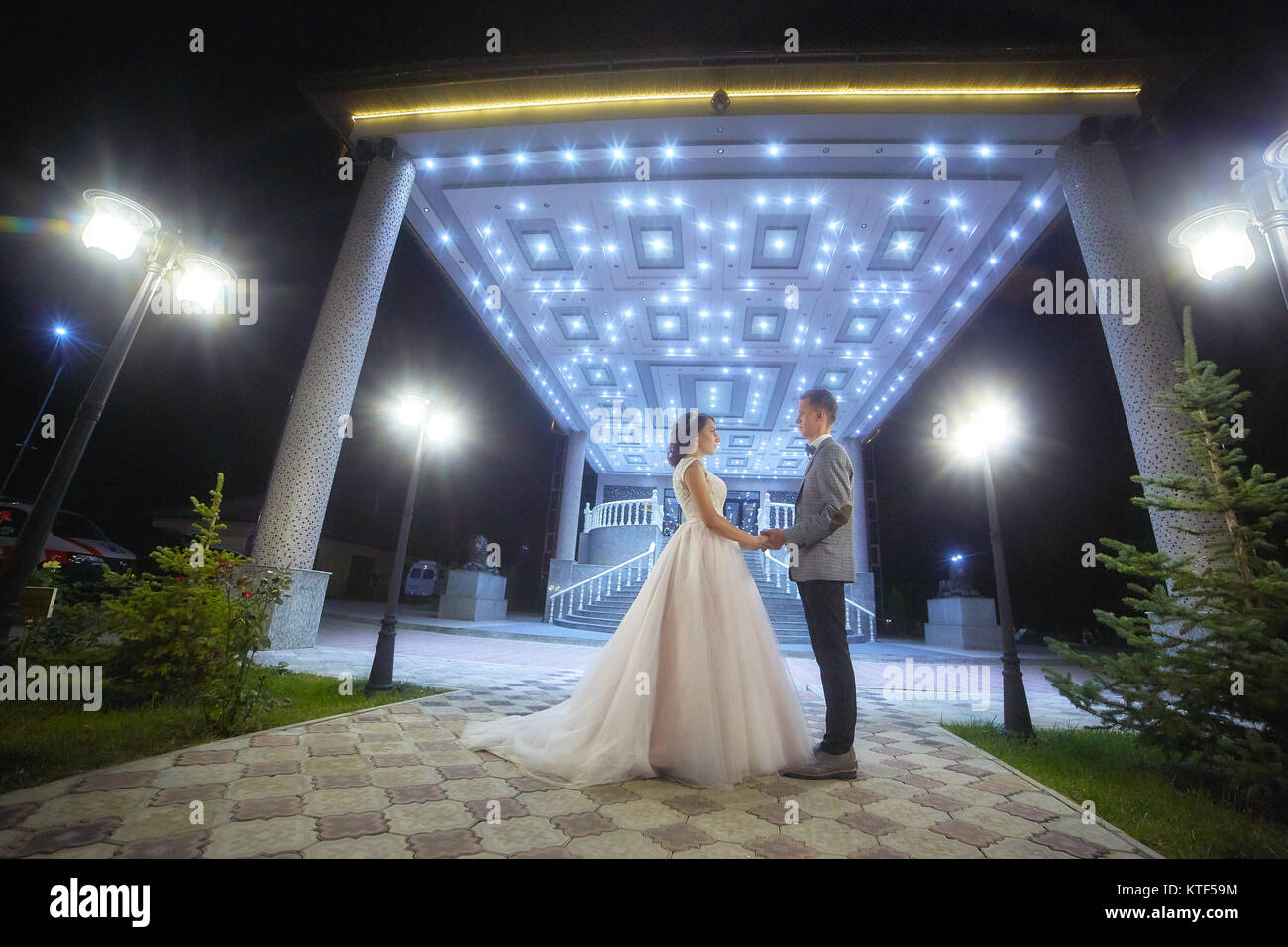 The bride and groom stand on the beautiful porch of the hotel at night