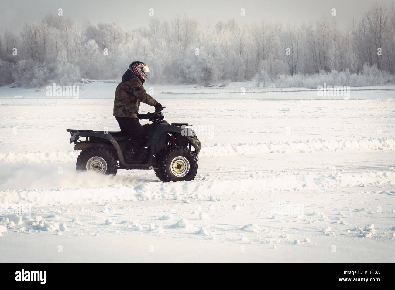 Winter fun on the ATV. A fisherman rides on the frozen lake in winter quartro bike on the background of beautiful winter landscape with snow-covered t Stock Photo