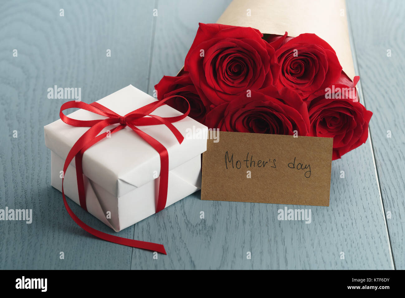 gift box with red roses bouquet and mothers day paper card on blue wood ...