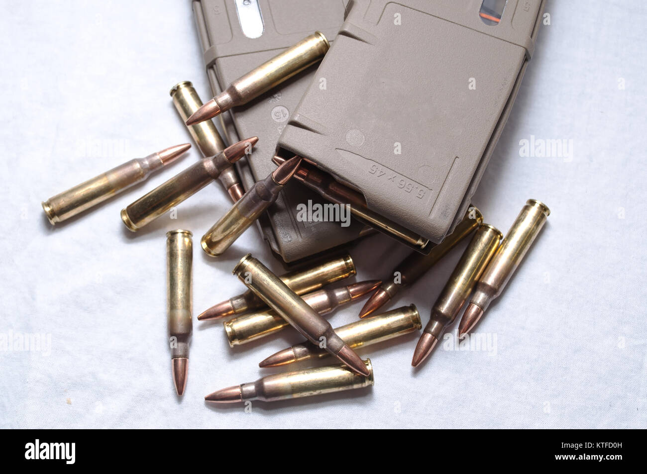 Two brown rifle magazines loaded with .223 rounds and several rounds laying next to them on a white background Stock Photo