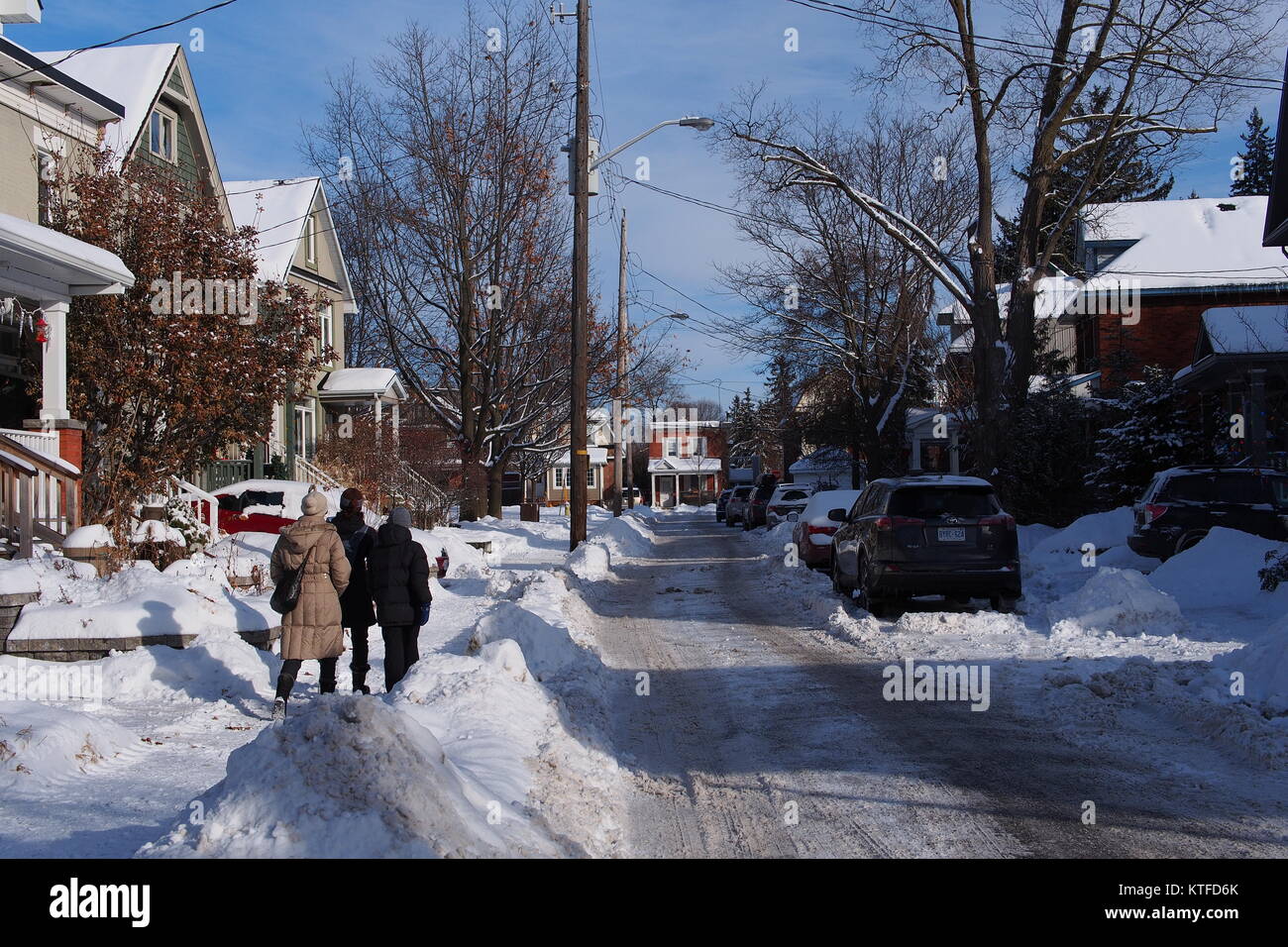 Three people walking down a Glebe street, after a fresh snowfall. Ottawa, Ontario, Canada. Stock Photo